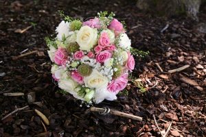 Brautstrauß in weiß-rosa und Eheringe auf Waldboden