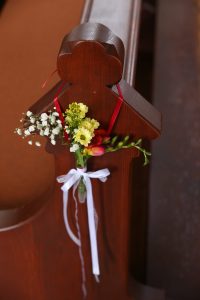Blumenanhänger an Kirchenbank mit rotem Band